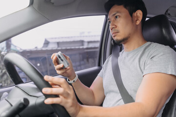Side view of asian man using mobile phone inside the car while driving on road, incautious, accident cause.