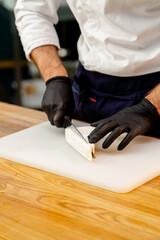 Fototapeta na wymiar close-up of a chef's hands in black gloves slicing cheese on table in the kitchen