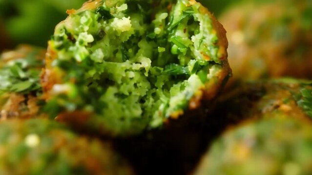 Closeup of a falafel crispy and golden brown on the outside revealing a vibrant green interior of chickpeas and herbs. The aroma of cumin and coriander wafts through the air. .