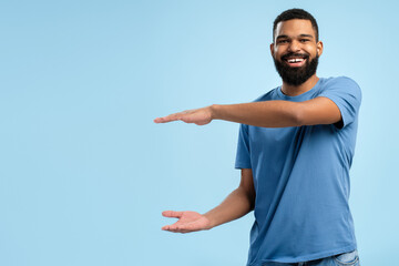 Smiling African American man pointing away side with hands over blue background with copy space