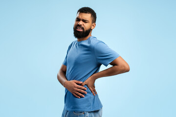 Upset African American man suffering from pain, muscle spasm over blue background