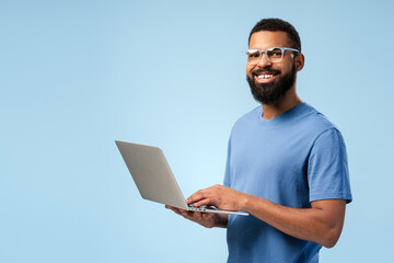 Smiling African American man in eyeglasses typing on the laptop while looking at camera
