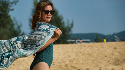A woman is walking on the beach wearing a green and white elephant print scarf