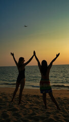 Two women are standing on the beach, one of them is wearing a black swimsuit