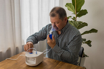 Elderly man sitting on a table and using a nebulizer mist at home