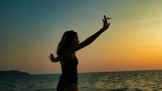 A woman standing on the beach. The other hands has a silhouette of an airplane is if she is pushing it away.