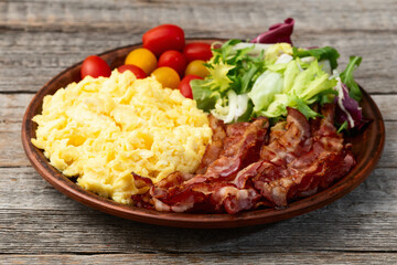 Breakfast plate . Scrambled eggs , bacon , cherry tomatoes and salad