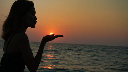 The silhouette of a woman, her figure cast in shadow, as if she is blowing the sun away from her...