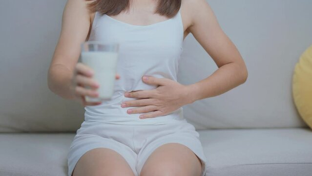 Lactose intolerance and Milk allergy concept. woman hold Milk glass and having abdominal cramps and pain when drink Cow Milk. Symptom stomach ache, Dairy intolerant, Nausea, Bloating, Gas and Diarrhea