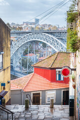 Street view of the narrow cobblestone streets of Porto with its old buildings and the Dom Luís I Bridge. Fragment of a metal railroad bridge, Portugal. - 789096407