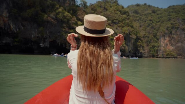 Woman sitting on boat passing lagoon. Back view female travel, riding on gondola, sitting on ship bow and looking take a photo of nature in a wicker hat in summer day. Tourism, adventure lifestyle.