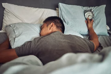 Gardinen Man, sleeping and bed with alarm clock or tired insomnia for bad time management, depression or dreaming. Male person, pillow and lazy snooze in home or overworked burnout, mental health or Monday © peopleimages.com