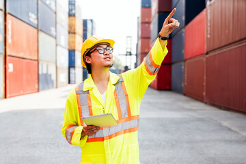 Asian man engineer working with tablet and point up at containers at a container yard. Shipping business management and international goods import-export. Logistic operation concept. Diversity workers