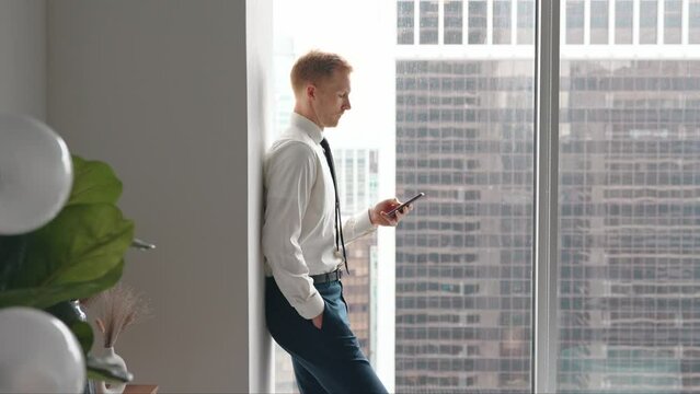 Busy professional business man standing in office holding cellphone. Young businessman entrepreneur using smartphone cell phone technology device looking at mobile at work.