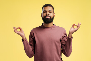 African American man relaxing with eyes closed, doing meditation gesture, over yellow background
