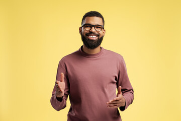 Happy young African American man wearing eyeglasses while posing in studio, over yellow background