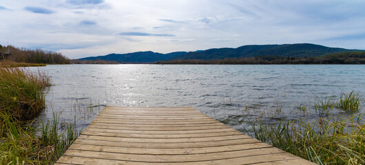 Un muelle de madera se extiende sobre las aguas del Lago Banyoles, ofreciendo una vista majestuosa...