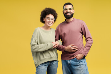African American couple in eyeglasses hugging while posing in studio, isolated on yellow background