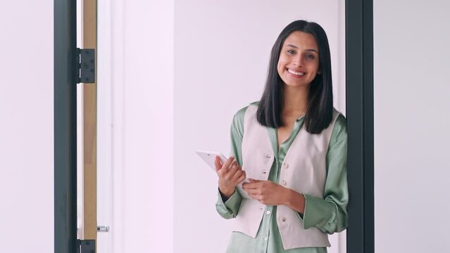 Young smiling professional Indian business woman, happy confident female company employee or student holding digital tablet standing in modern office at worki, looking at camera, portrait.