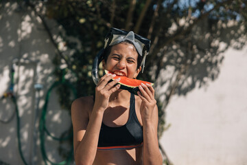 Latina teenage girl eating a slice of watermelon while taking a play break at the pool
