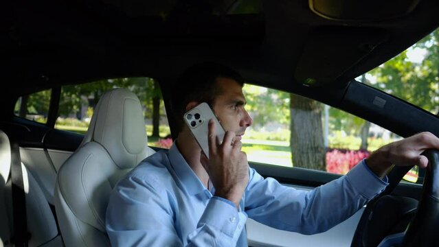 Profile of confident businessman driving electric car on urban road and talking on phone. Male businessperson operating electrical vehicle at city and speaking by smartphone. Concept of business