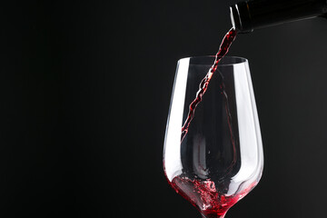 Obraz premium Pouring red wine into glass against black background, closeup. Space for text