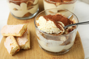 Delicious tiramisu in glasses, cookies and spoon on white table, closeup