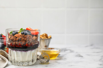 Tasty granola with berries, jam and yogurt in glass on white marble table, space for text