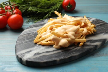 Delicious French fries with cheese sauce, tomatoes and dill on light blue wooden table, closeup
