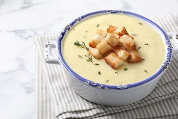 Tasty potato soup with croutons and rosemary in ceramic pot on white marble table, space for text