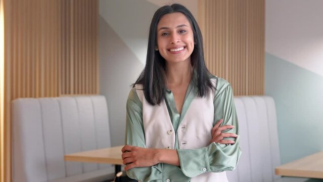 Young confident happy Indian business woman looking at camera in corporate office. Professional businesswoman employee, female entrepreneur standing arms crossed thinking of new goals. Portrait.