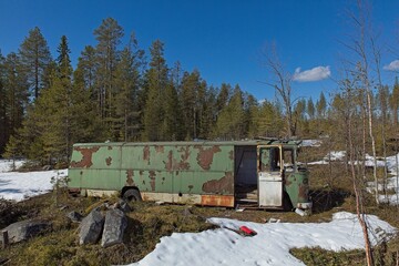 Old abandoned green bus in forest in clear spring weather with snow on the ground.