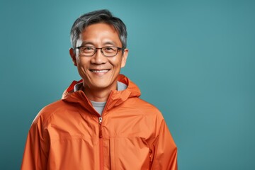 Portrait of a satisfied asian man in his 50s wearing a lightweight packable anorak over solid color backdrop - obrazy, fototapety, plakaty