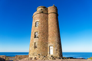 L'ancien phare du Cap Fréhel, emblème chargé d'histoire des Côtes d'Armor, trône majestueusement sur la côte bretonne, rappelant la grandeur passée de la navigation maritime dans la région. - obrazy, fototapety, plakaty