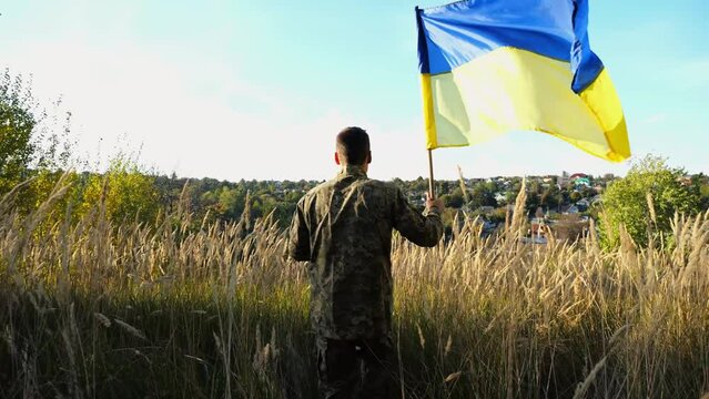 Male soldier of ukrainian army runs with lifted blue-yellow banner outdoor. Young man in military uniform waving flag of Ukraine at countryside. Concept of russian invasion resistance. Slow motion