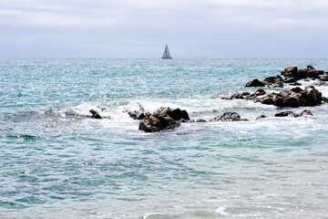 View to shore with waves crashing on rocks in background on horizon sailing boat sailing.
