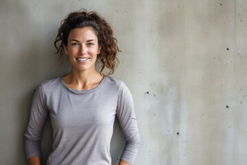 Portrait of a cheerful woman in her 30s wearing a moisture-wicking running shirt isolated on bare concrete or plaster wall