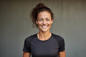 Portrait of a cheerful woman in her 30s wearing a moisture-wicking running shirt isolated in bare concrete or plaster wall