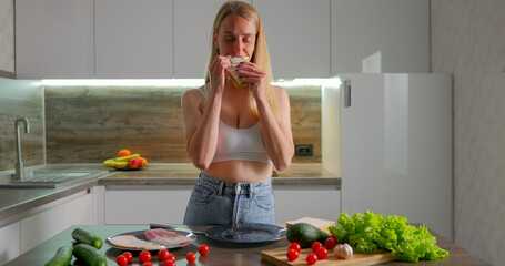 Young woman eating selfmade sandwich with lettuce and ham at home