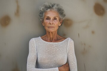 Portrait of a tender woman in her 80s sporting a long-sleeved thermal undershirt in bare concrete or plaster wall