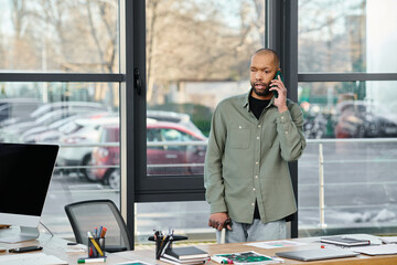 A man with myasthenia gravis in business attire talking on a cell phone while standing in front of a desk in an office setting.