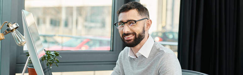 A man in a corporate setting sits at his desk, focused on his computer screen.