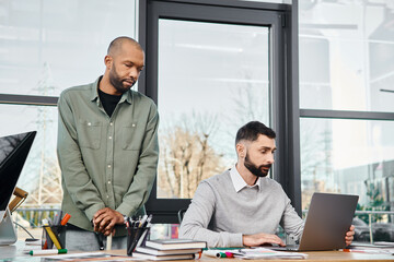 Two men engrossed in laptop, brainstorming ideas, working on a project in a modern office setting.