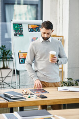 A man relaxes at a table with a cup of coffee in a bustling office environment, taking a moment to regroup amidst corporate hustle.