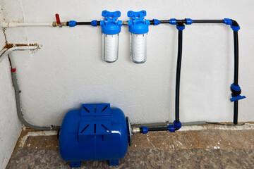 String wound cartridge filters and water storage pressure tank are connected to domestic water supply in utility room of residential.