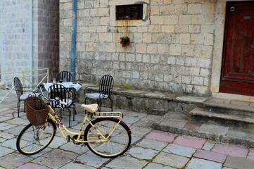 A lady's old yellow bicycle with a basket at the door of the house, a table with armchairs in the background