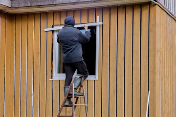 Exterior finishing of plastic window in frame-panel wooden country house, construction worker...