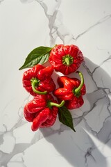 Fresh red habanero peppers with green leaves on a marble background