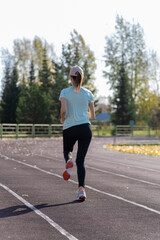 A young beautiful woman in sportswear plays sports at a local stadium. Exercise, jog and exercise at the beginning of the day. Healthy and active lifestyle.