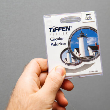 Paris, France - Jan 3, 2018: Man hand holding against gray background professional Tiffen Circular Polarizer filter for 77mm diameter camera lens